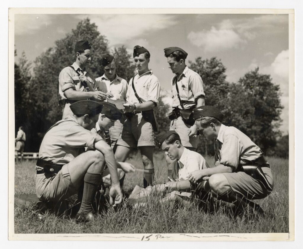 Student pilots stand and crouch in a circle outdoors, studying their target sheets.